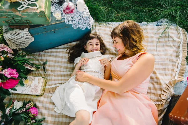 Счастливые мать и дочь играют и улыбаются, лежа на одеяле летом — стоковое фото
