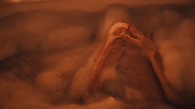 çıplak esmer kız cinsel bacaklarını okşur ve şampanya bir bardak köpük ile banyoda sahiptir