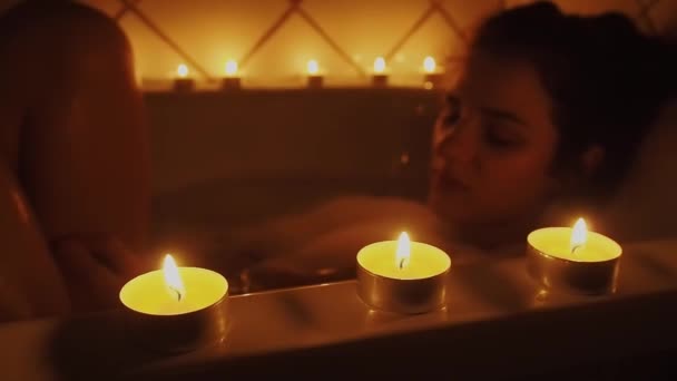 Beautiful young brunette girl resting in the bathroom with candles — Stock Video