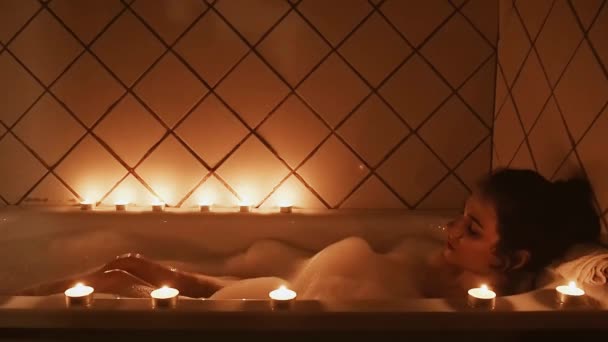 Young girl relaxes in the bath by candlelight and blows off the foam — Stock Video