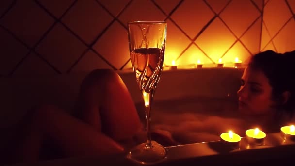 Glas Champagne met kaarsen op de achtergrond van een wazig ontspannend jong meisje in de badkamer — Stockvideo