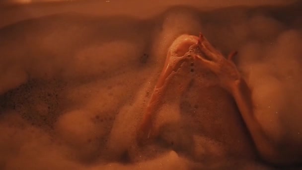 Naga brunetka dziewczyna seksualnie pieszczoty jej nogi i cieszy się w łazience z pianki z kieliszkami szampana — Wideo stockowe