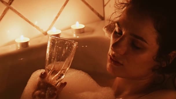 赤裸裸的黑发女孩喜欢在浴室泡沫与一杯酒精饮料香槟在她的手中的蜡烛光 慢动作 — 图库视频影像