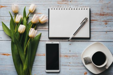 Lale kahve fincanı, smartphone ve boş defter ile ahşap arka plan üzerinde beyaz buket