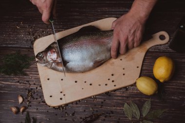 Erkek Şef mutfak ahşap bir yönetim kurulu ham alabalık keser. Yemek pişirmek için çiğ balık