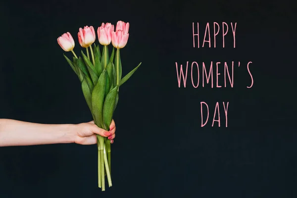 Tarjeta de felicitación con la inscripción feliz día de la mujer. Ramo de flores de tulipán rosa en la mano de una mujer — Foto de Stock