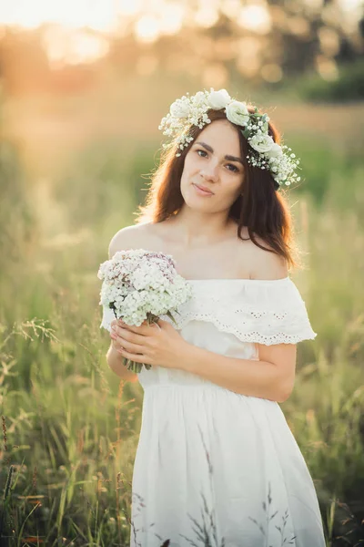 Kaukázusi boldog lány egy fehér ruhában, egy csokor virágot és egy koszorú, nyáron — Stock Fotó