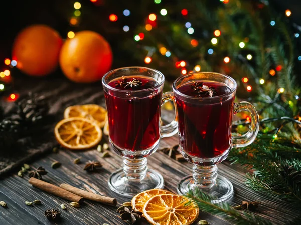 Vino caliente en copas sobre la mesa decorado con un árbol de Navidad. Rodajas de naranja, estrellas de anís, cardamomo, canela — Foto de Stock