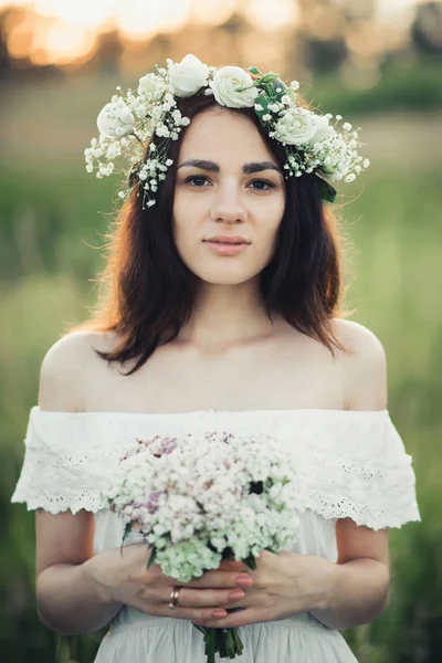 Portret z atrakcyjną dziewczyną w białej sukni z bukietem kwiatów i wieniec w lecie — Zdjęcie stockowe