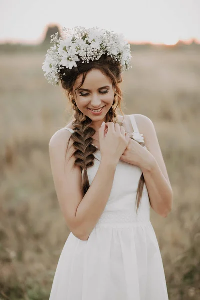 Gelukkig lachend meisje met vlechten en bloemen krans in witte jurk in boho stijl in de zomer buiten — Stockfoto