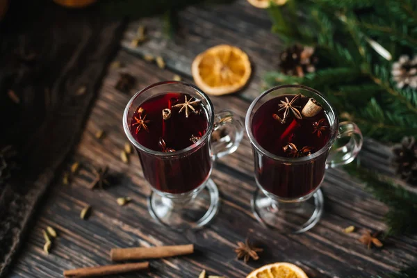 Δύο ποτήρια με ζεστό κρασί με φέτες πορτοκαλιού και κανέλα, κάρδαμο σε ξύλινο τραπέζι — Φωτογραφία Αρχείου