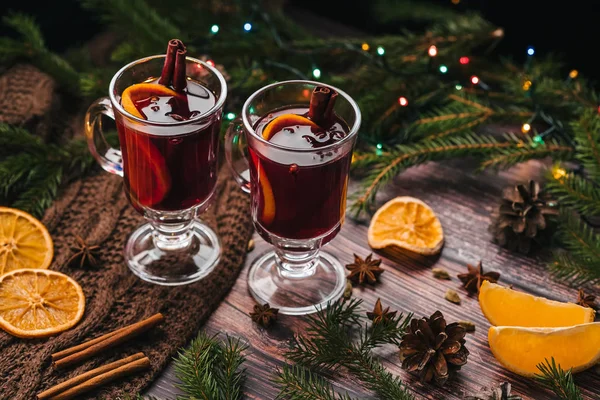 Δύο ποτήρια με mulled κρασί σε ένα ξύλινο τραπέζι με πορτοκάλι, κανέλα, κάρδαμο, γλυκάνισο αστεριών. Παραδοσιακό χειμώνα ζεστό αλκοολούχο ποτό — Φωτογραφία Αρχείου