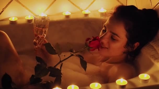 Elinde bir gül ile köpük ile banyoda yatan mutlu güzel genç kız ve şampanya içme — Stok video