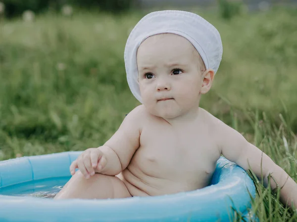 Menino sentado em uma piscina inflável azul em um dia de verão — Fotografia de Stock