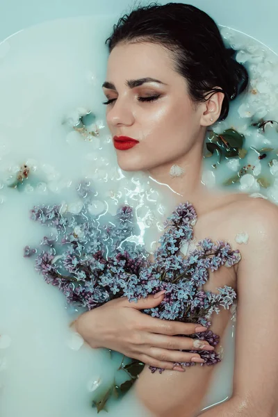 Retrato de beleza de uma bela jovem em um banho com leite e flores de lilás — Fotografia de Stock