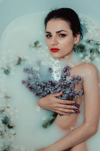 Retrato de beleza de uma bela menina nua em um banho com leite e flores de lilás — Fotografia de Stock