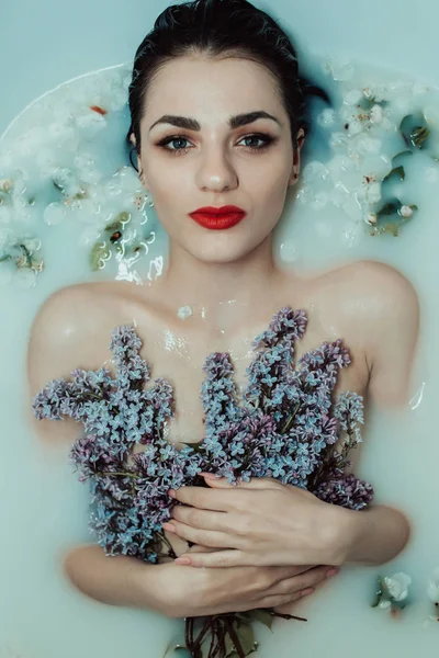 Bela menina nua com batom vermelho e maquiagem relaxante e descansando no banho com leite e lilás e flores de maçã — Fotografia de Stock
