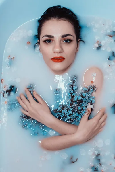 Retrato de uma jovem menina sexy com um buquê de lilases relaxante e desfrutando no banho com leite e flores — Fotografia de Stock
