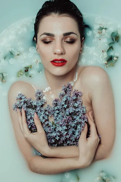 Jovem sexy caucasiano menina com um buquê de lilases no banho com leite e flores — Fotografia de Stock
