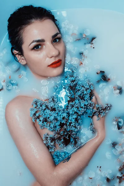 Jovem sexy menina com um buquê de lilases relaxar e desfrutar no banho com leite azul e flores — Fotografia de Stock