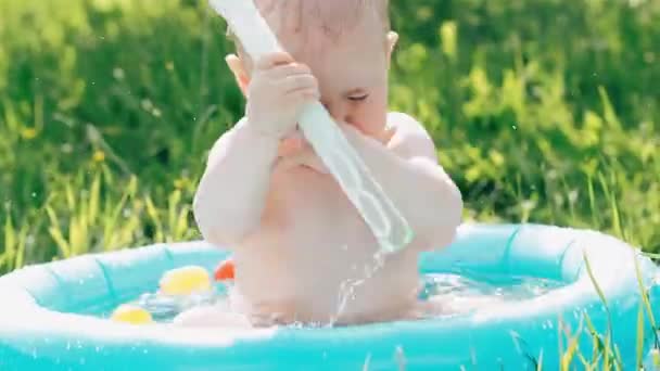面白い感情的な少年の子供が飛び散り、青いインフレータブルプールで水しぶきで遊ぶ — ストック動画