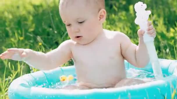 Kleine baby jongen is zwemmen en plezier spelen met water spatten in het Opblaasbare zwembad op een zomer — Stockvideo