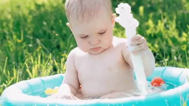 Kleine schattige baby jongen spelen en spatten water druppels in opblaasbare zwembad op gazon op de zomer — Stockvideo