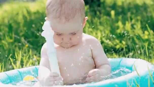 Little boy baby playing with water splashes in inflatable pool on lawn on summer day — Stock Video