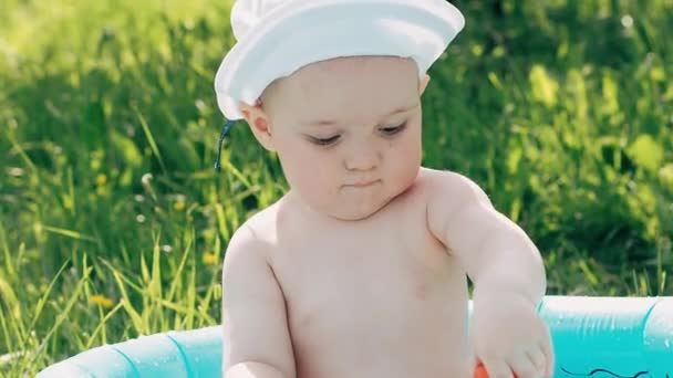 Щасливий маленький хлопчик, який грає з іграшками в надувному басейні на газоні — стокове відео