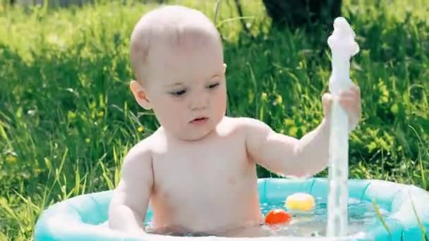 Liten pojke barn leker och ler i den uppblåsbara poolen på en sommardag — Stockvideo