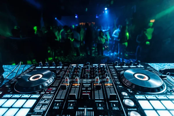 Mezclador de DJ de música profesional en un stand en un club nocturno en el fondo de siluetas borrosas de personas bailando —  Fotos de Stock