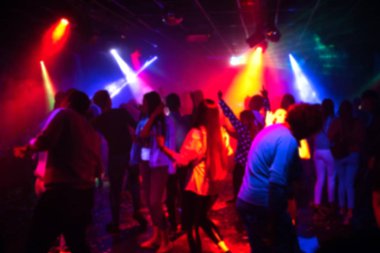renkli spot ışıkları altında dans pistinde bir gece kulübünde dans eden bir grup insanın bulanık siluetleri