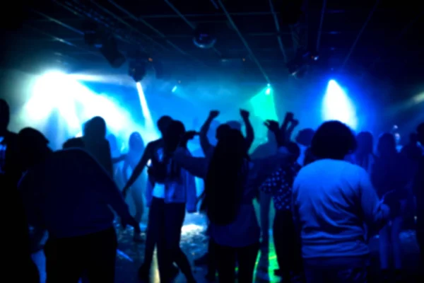 Θαμπές σιλουέτες μιας ομάδας ανθρώπων που χορεύουν σε ένα νυχτερινό κέντρο διασκέδασης στην πίστα κάτω από πολύχρωμους προβολείς — Φωτογραφία Αρχείου