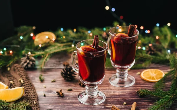 오렌지, 계피, 카르다몸, 크리스마스 트리와 화환으로 장식된 테이블에 있는 아니스 별이 있는 유리 잔에 드린 와인 — 스톡 사진