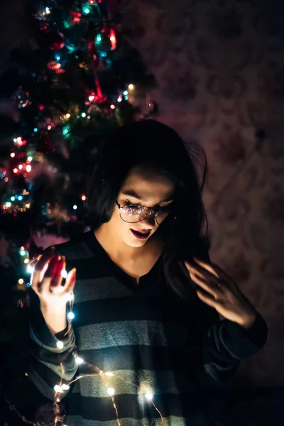 Meisje met glazen houden een slinger met lichten 's nachts thuis — Stockfoto