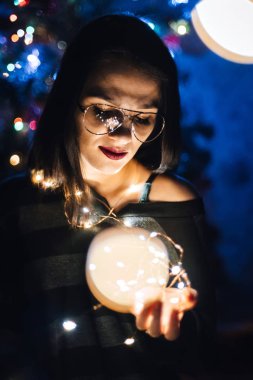 evde geceleri ışıklar ile bir çelenk tutan gözlüklü kız