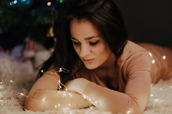 Felice ragazza bruna attraente sdraiata a casa vicino all'albero di Natale — Foto Stock