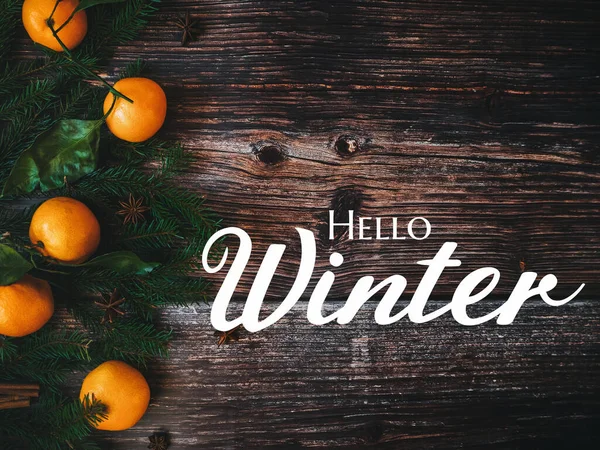 text Hello Winter on a wooden background with fir branches and mandarins