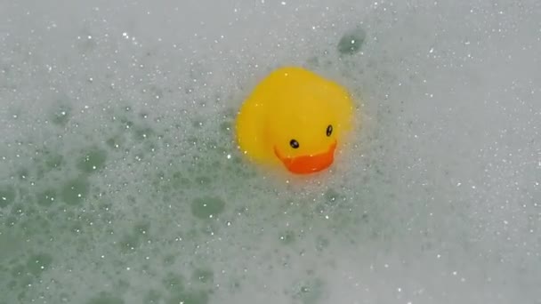 Rubber yellow duck toy floats in water in bath with foam — Αρχείο Βίντεο