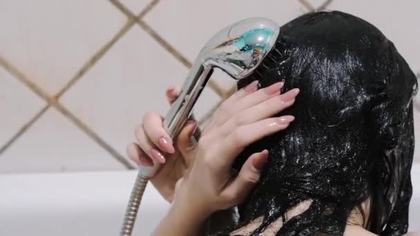 Junge brünette Mädchen wäscht das Shampoo aus den Haaren mit Wasserdusche im Badezimmer — Stockvideo