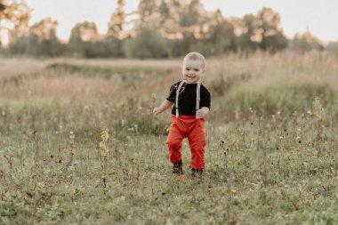 Komik küçük çocuk çimenlerde koşuyor ve yaz tarlasında gülümsüyor.
