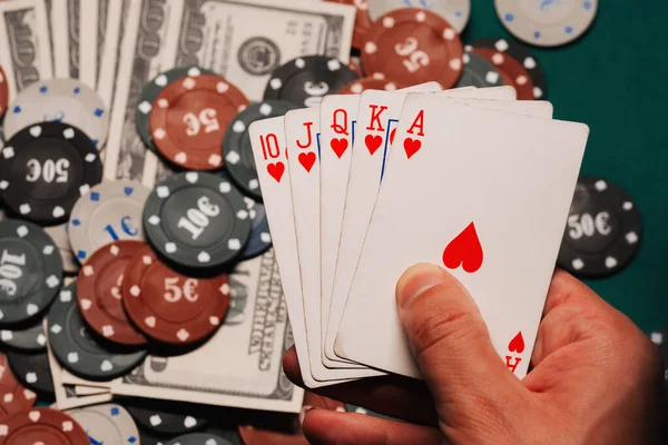 Royal flush in poker in the hands of the player on the background of gaming chips and money