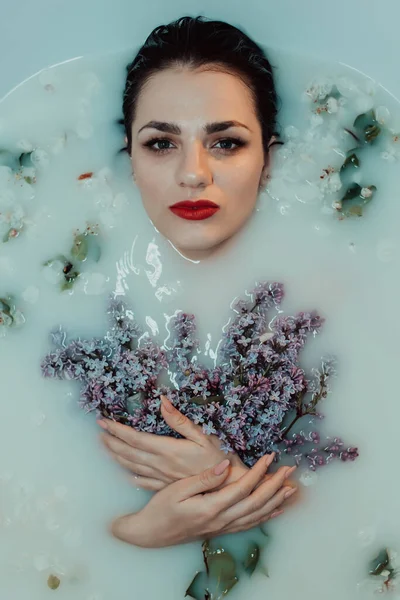 Retrato de uma menina bonita com batom vermelho e maquiagem relaxante e descansando no banho com leite e lilás — Fotografia de Stock
