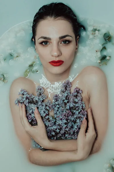 Retrato de uma jovem caucasiana com um buquê de lilases no banho com leite e flores — Fotografia de Stock