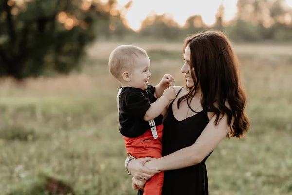 Joven madre blanca con hijo en sus brazos sonriente y feliz en el campo de verano —  Fotos de Stock
