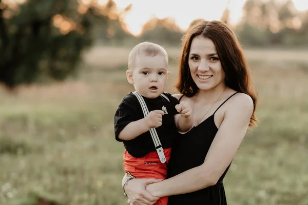 Joven feliz mamá sonríe sosteniendo a su hijo en sus brazos en el verano en el campo —  Fotos de Stock