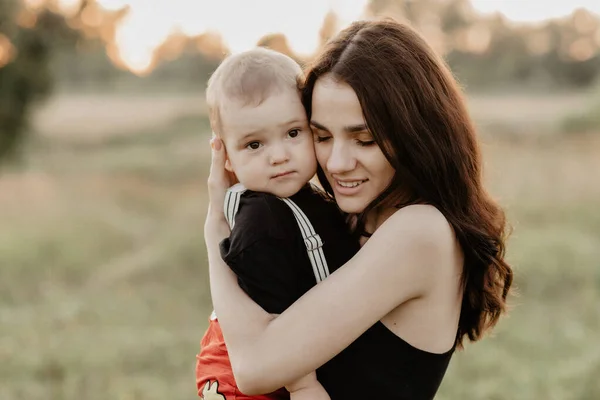 Joven madre caucásica sonríe abrazando a su pequeño hijo en el verano en un campo en la naturaleza —  Fotos de Stock