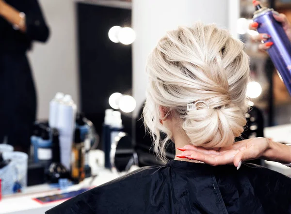 Cabeleireiro faz suas próprias mãos penteado um pão na cabeça de uma menina loira — Fotografia de Stock