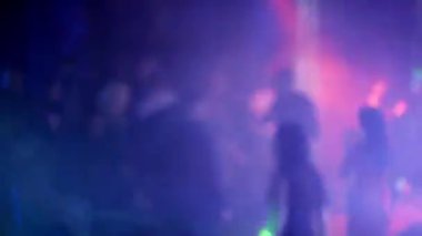 Bir gece kulübünün dans pistinde dans eden kalabalığın bulanık silüetleri.