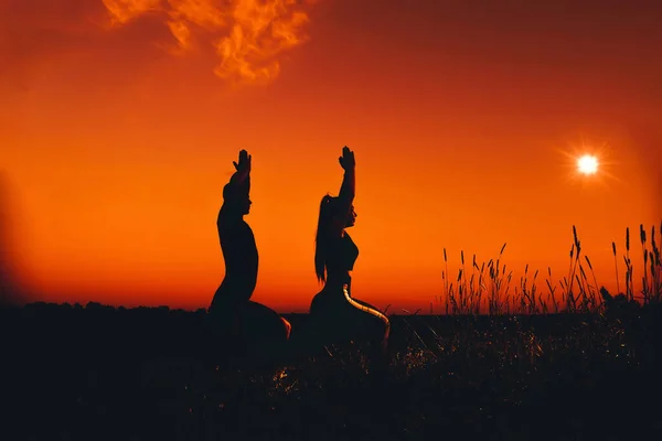 Silhouette d'un couple de personnes dans une pose de yoga au coucher du soleil — Photo